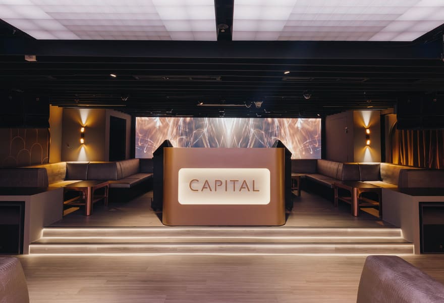 Lounge venue stage with DJ booth labeled Capital, booth seating, and ambient lighting