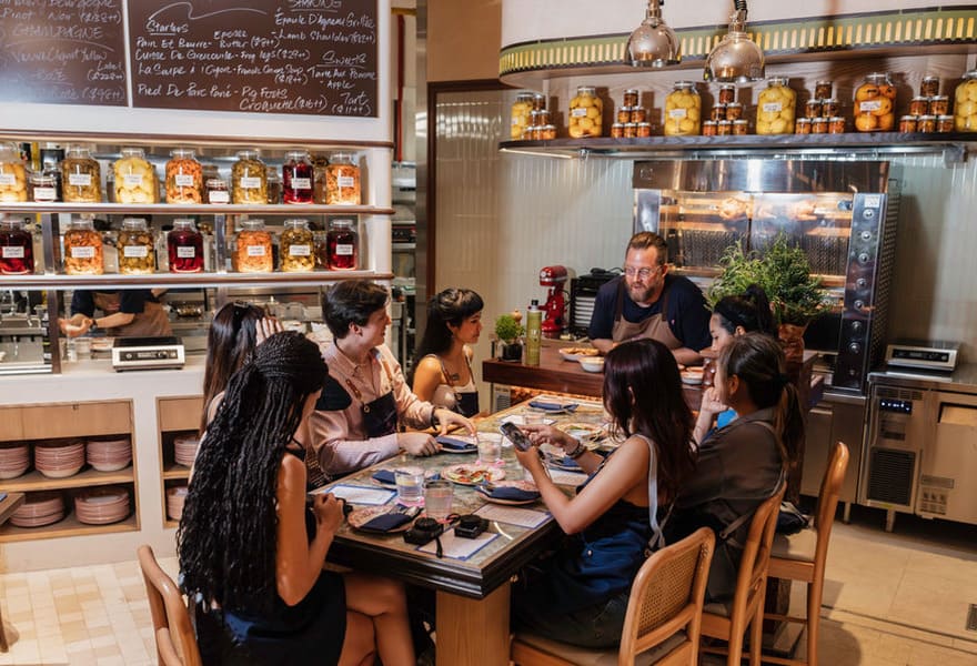 Cooking class setting with chef instructing guests seated around a table in a kitchen