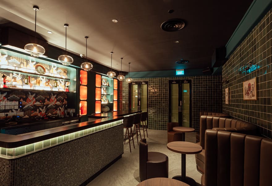 Intimate bar interior with tiled walls, booth seating, and illuminated back bar