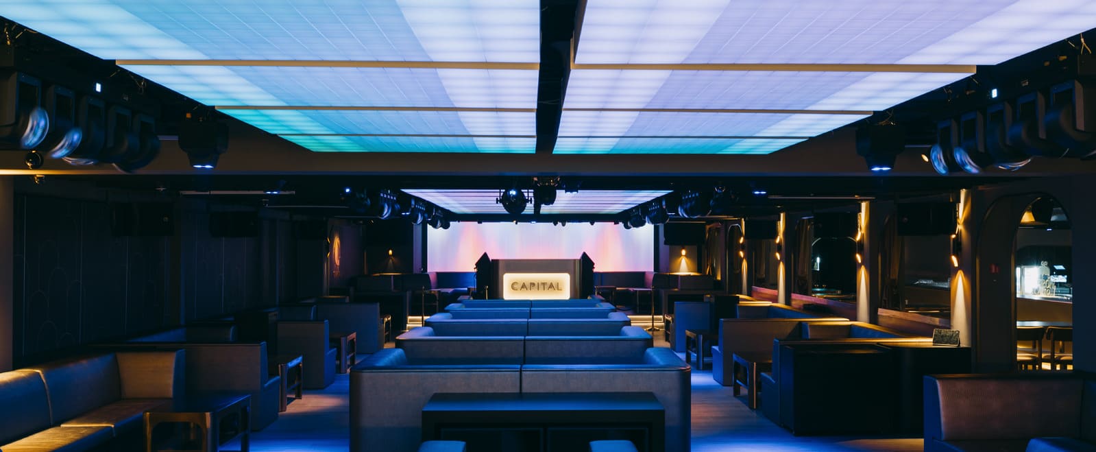 Modern lounge interior with booth seating, stage, and illuminated ceiling panels