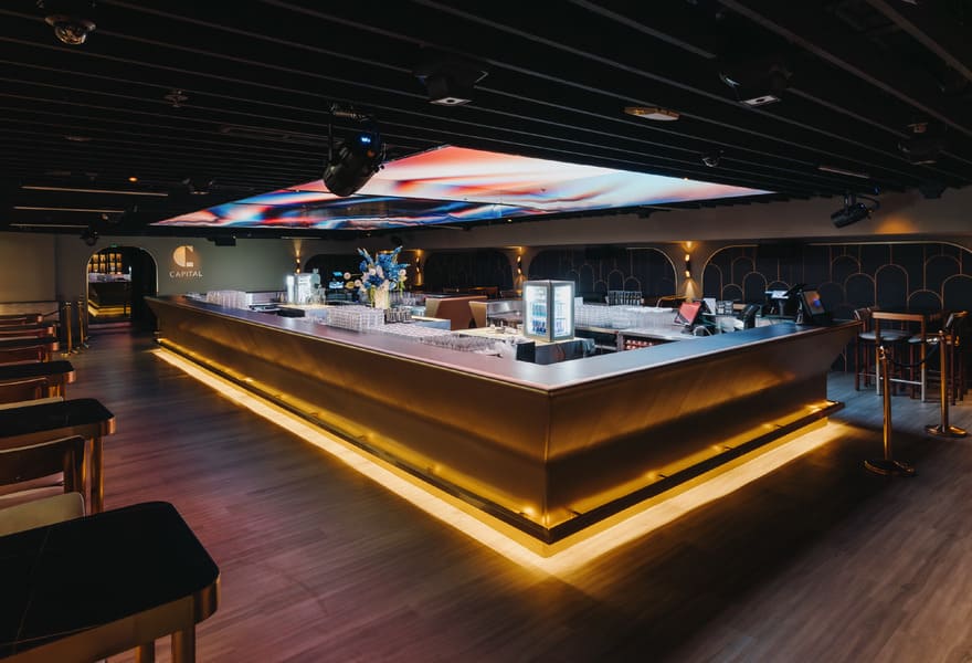 Modern nightclub bar with illuminated counter, seating area, and ambient ceiling lighting