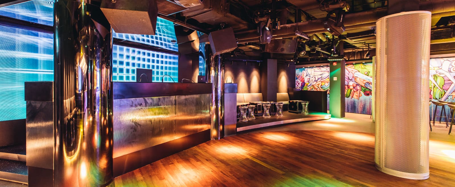 Nightclub interior with DJ booth, colorful lighting, LED wall, and seating area