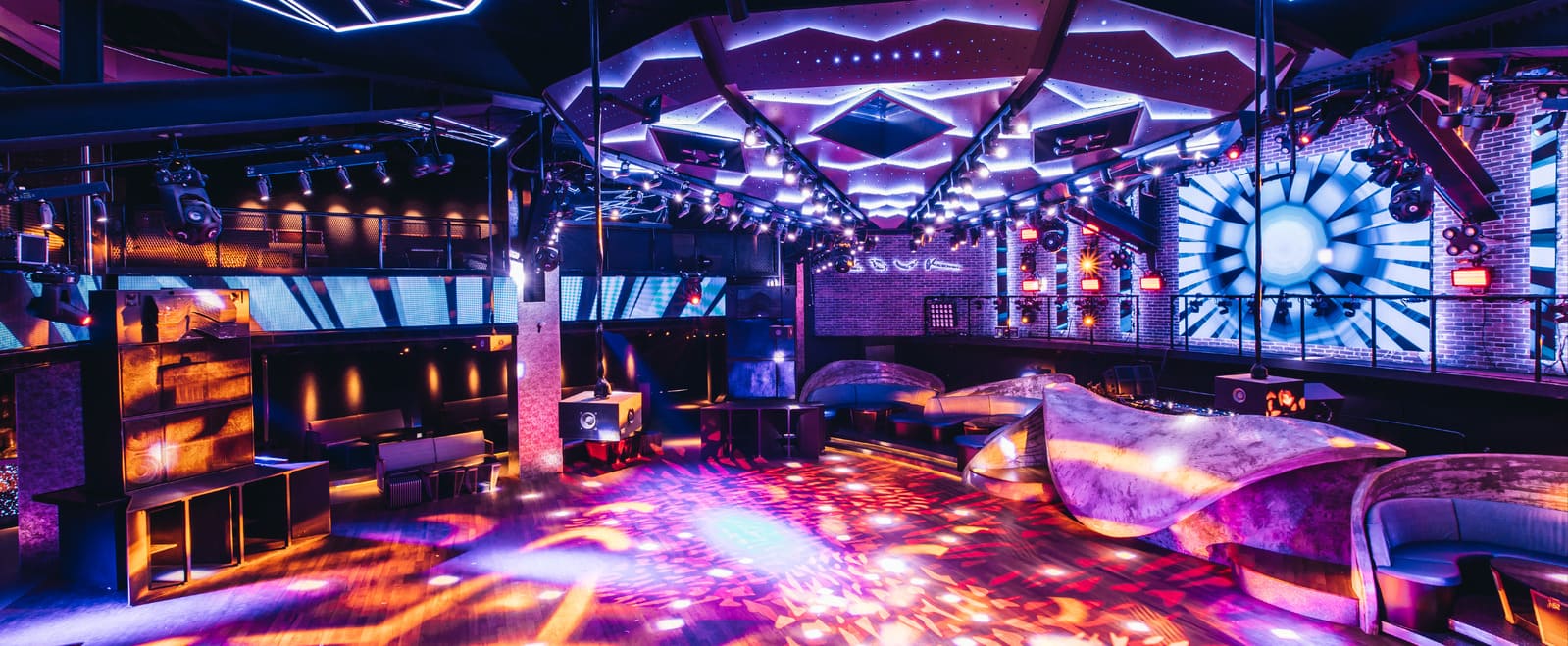 Empty nightclub interior with colorful lighting, dance floor, LED screens, and seating areas