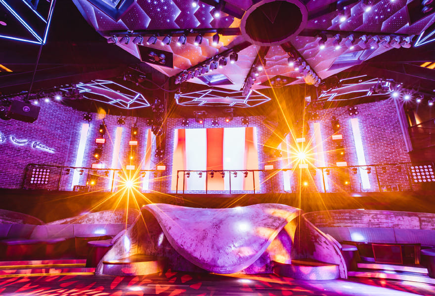 Nightclub stage with bright LED screens, colorful lighting effects, and illuminated dance floor
