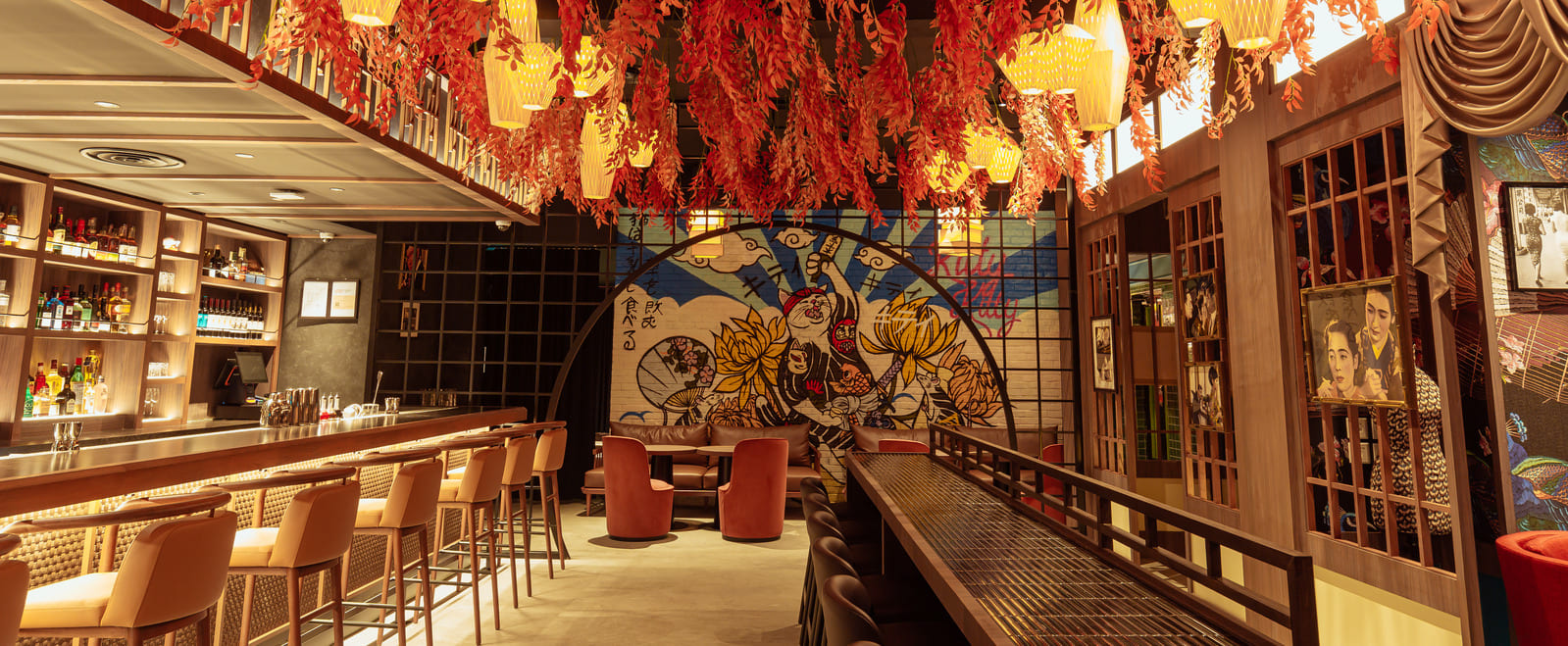 Restaurant interior with bar seating, hanging red decor, lantern lighting, and mural artwork