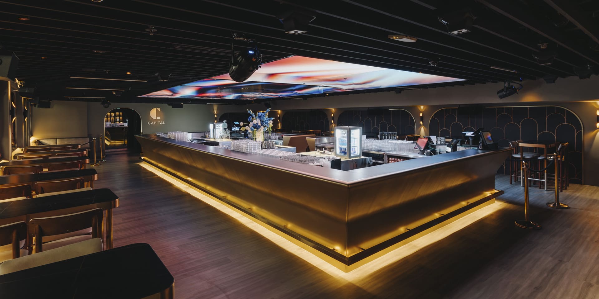 Modern island bar at Capital featuring illuminated counters, contemporary seating, and a large digital ceiling display in an upscale lounge setting.