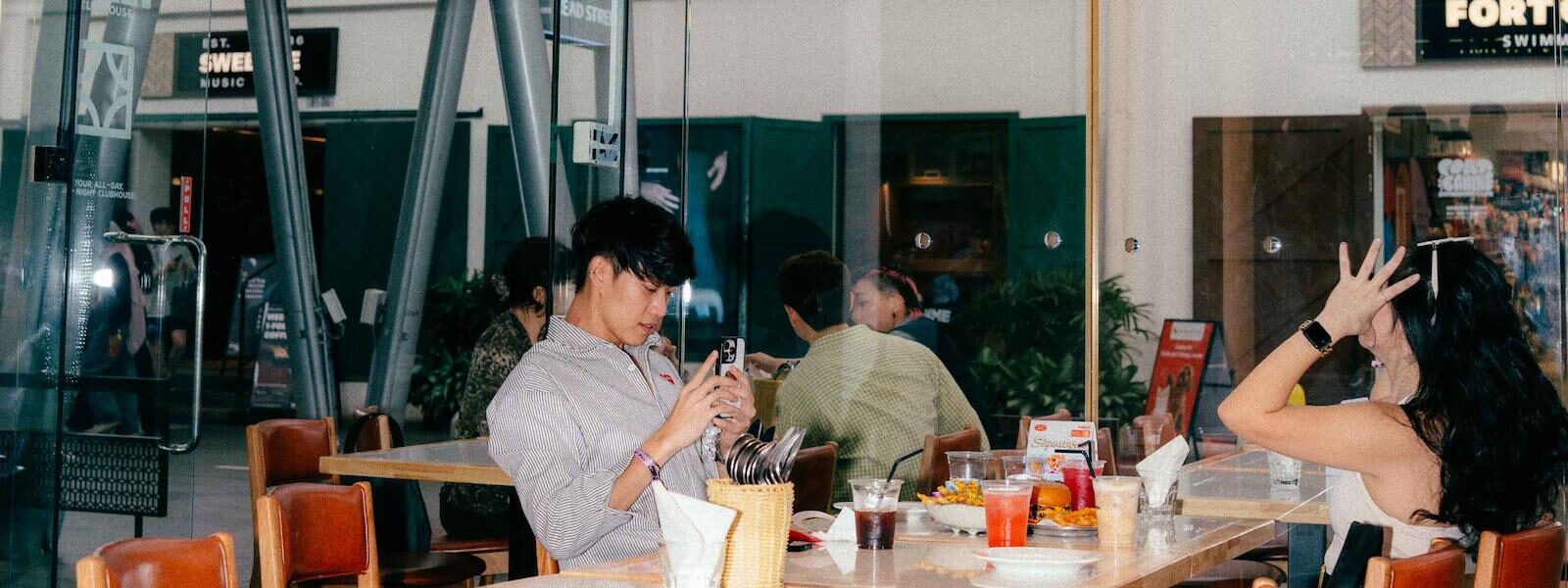 Guests dining in Rally House's bright modern dining room featuring large iridescent hanging spheres, floor-to-ceiling windows, and contemporary wood tables and chairs.