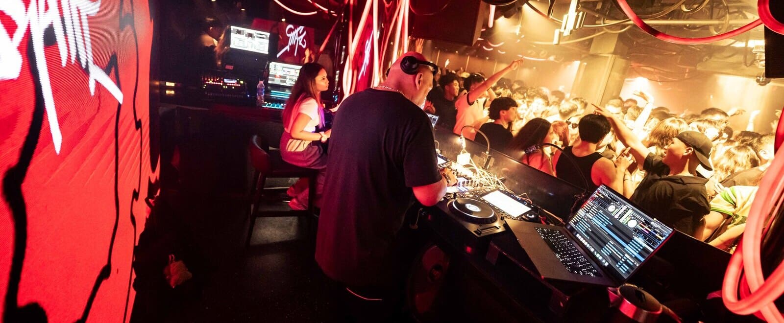 DJ performing inside Zouk's Phuture nightclub as a packed crowd dances beneath vibrant red lighting and LED displays surrounding the DJ booth.
